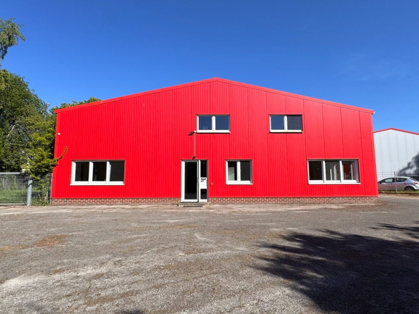 Firmen Gebäude Rote Fertigungshalle mit großen Fenstern und klarblauem Himmel im Hintergrund.